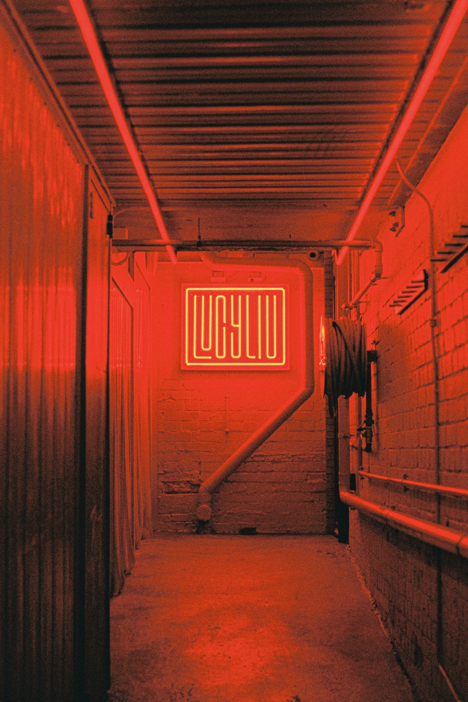 A red-lit alleyway leads to a neon sign that reads "LUCYLIU" on a brick wall.