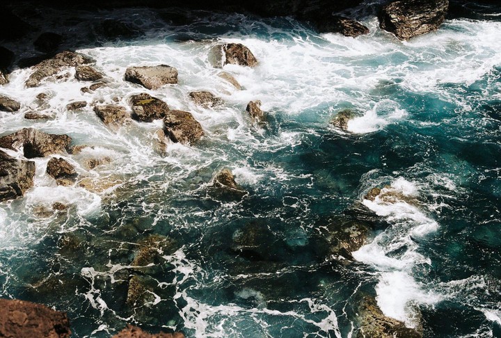 Waves crash against rocks along a coastline.