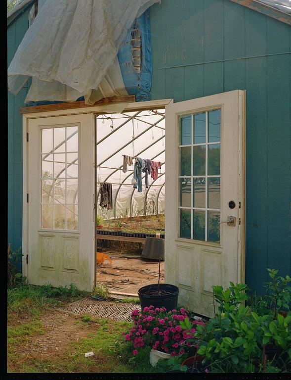 Two white doors open into a greenhouse where clothes are hanging to dry.