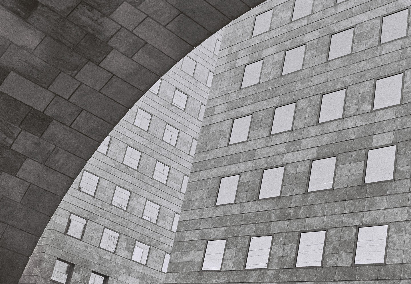 A brick archway frames two modern buildings with many windows.