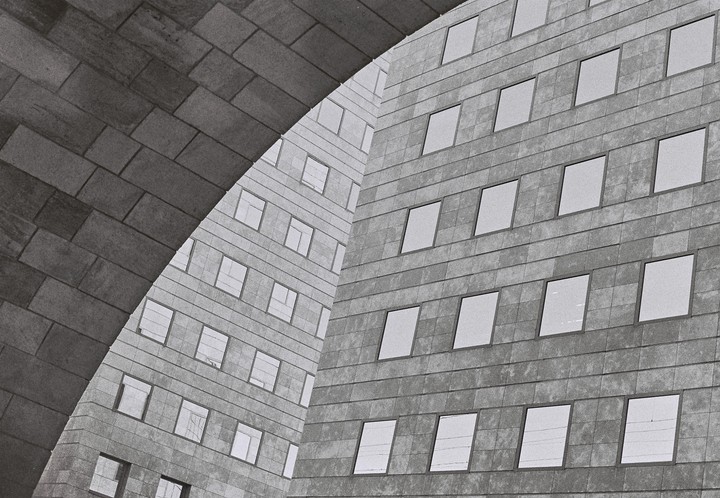 A brick archway frames two modern buildings with many windows.