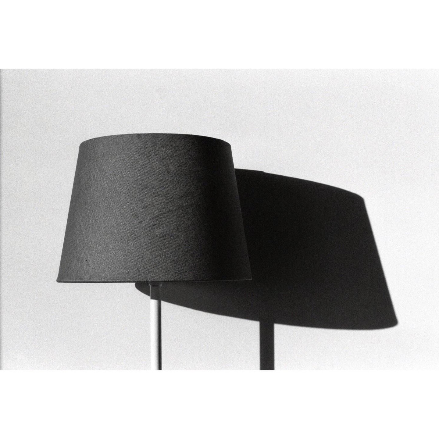 A black lampshade casts a large shadow on a white wall.