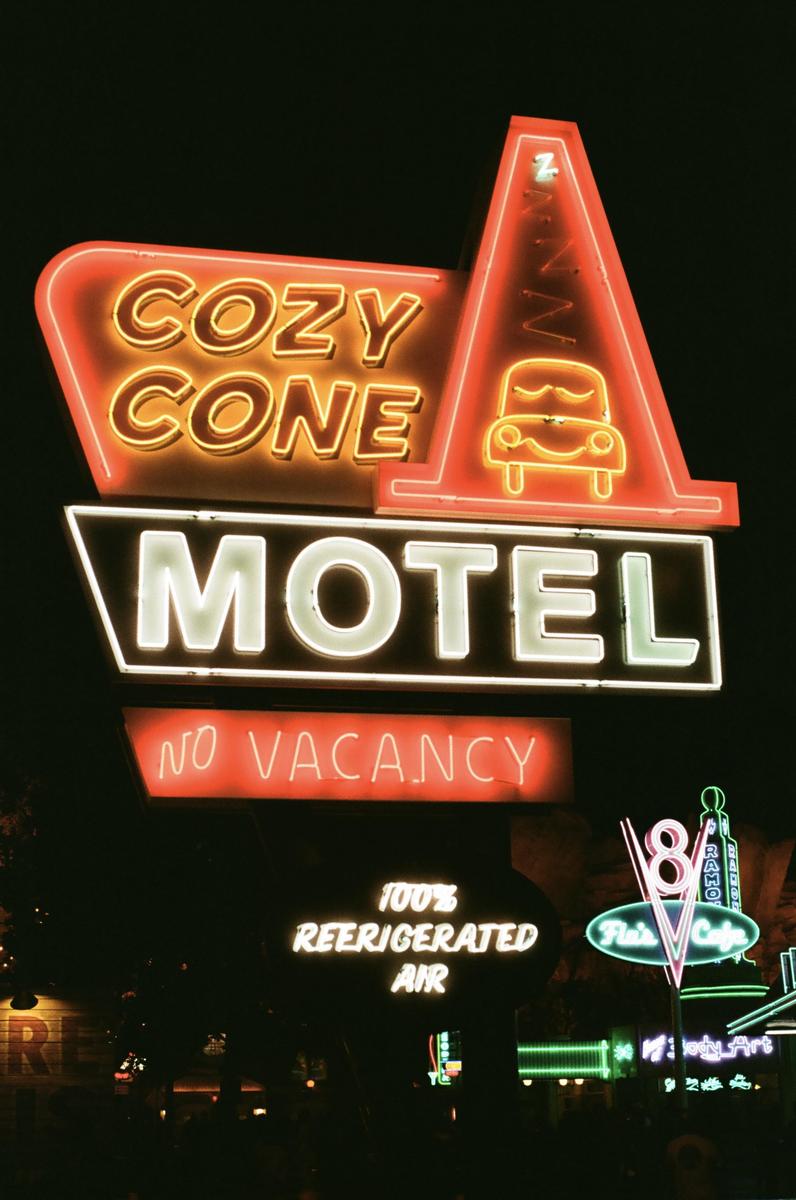 A neon sign for the Cozy Cone Motel with a sleeping car icon is illuminated at night.