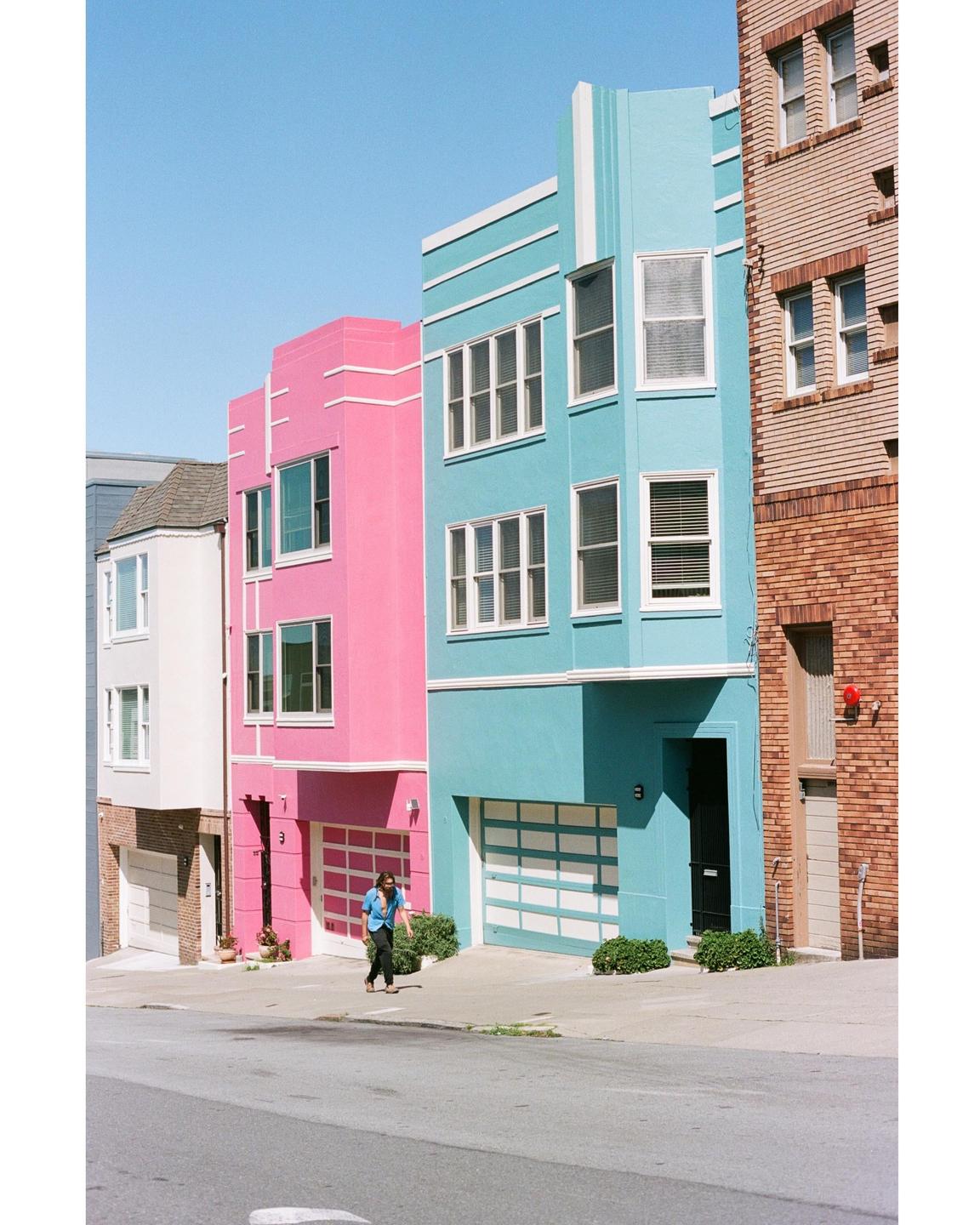 A woman walks past colorful houses on a sunny street in San Francisco.
