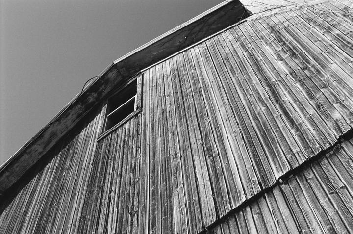 A low-angle view shows the weathered wooden side of a barn with a single window.