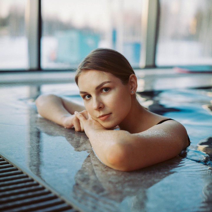 A woman rests her arms on the edge of a swimming pool, looking directly at the viewer.