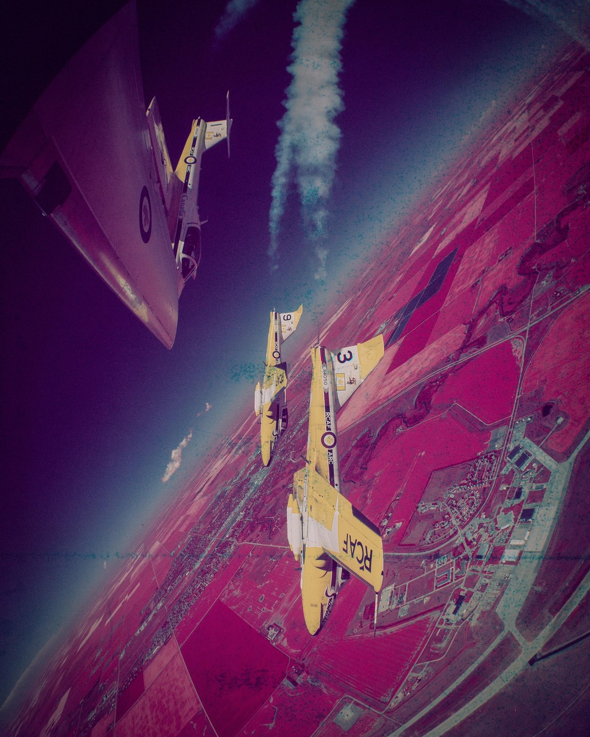 Three airplanes fly in formation over a landscape of red fields and a small town.
