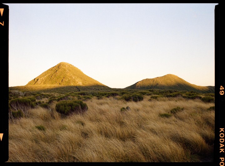 Two hills are visible in a field of tall grass under a clear sky.