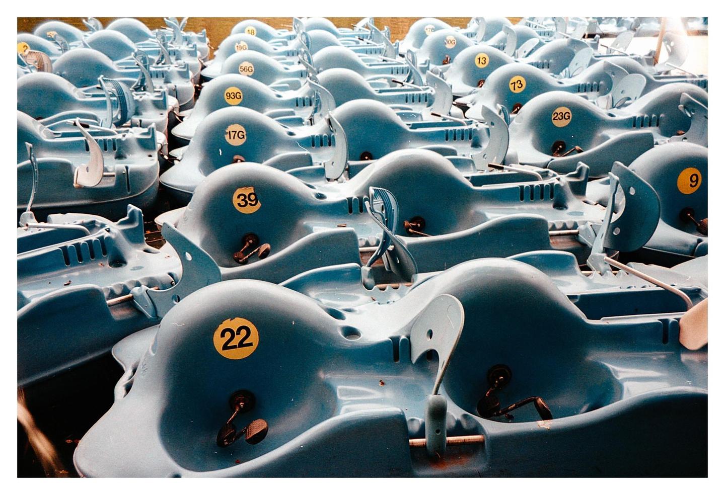 Many blue pedal boats with yellow numbers are docked together.