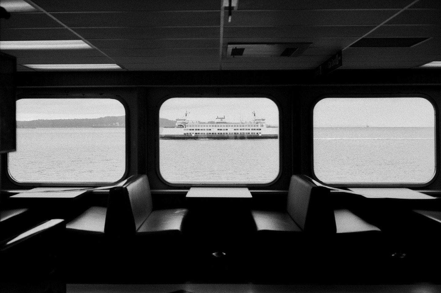 A ferry is visible through the windows of another ferry, which has empty booths and tables in the foreground.