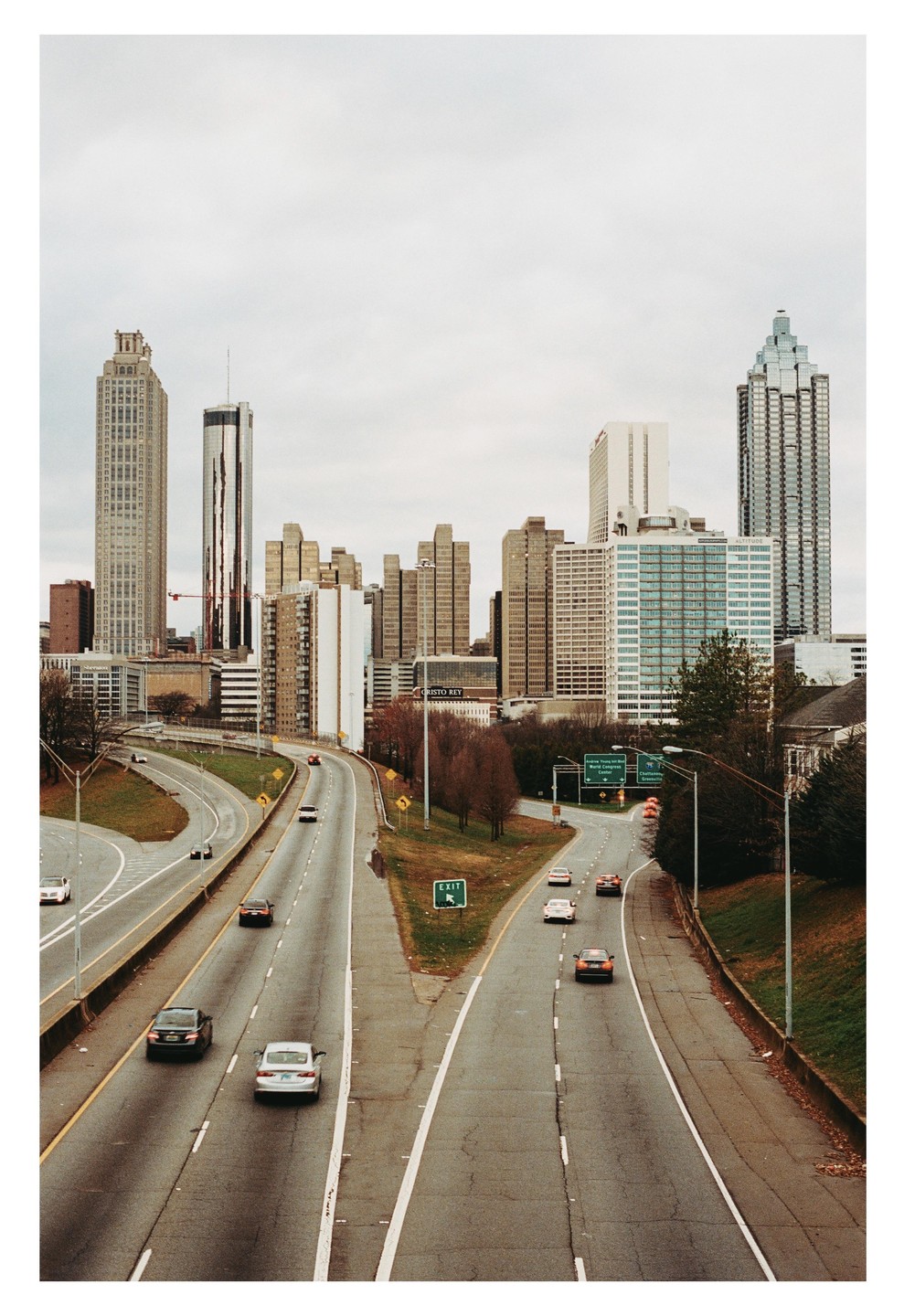 A highway with cars on it leads to a city skyline with tall buildings under a cloudy sky.