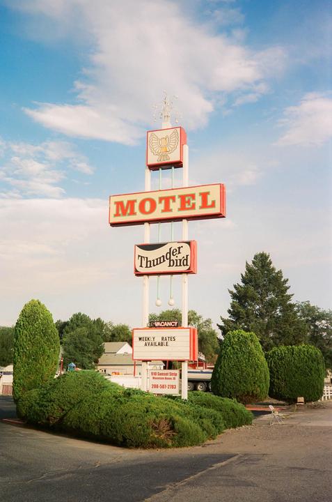 A tall motel sign with "Motel Thunderbird" written on it stands against a blue sky with clouds.