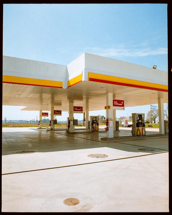 A gas station with multiple pumps stands under a bright blue sky.
