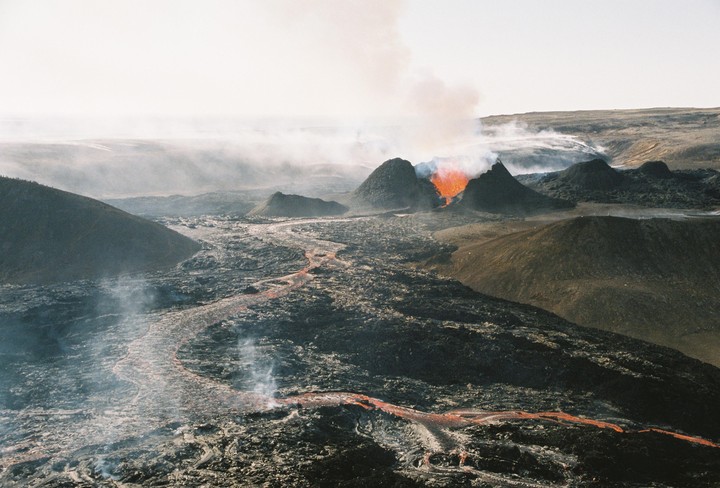A volcanic landscape shows a river of lava flowing from a volcano.