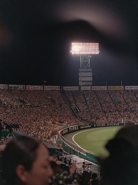 A baseball stadium is filled with spectators at night, illuminated by a large scoreboard.
