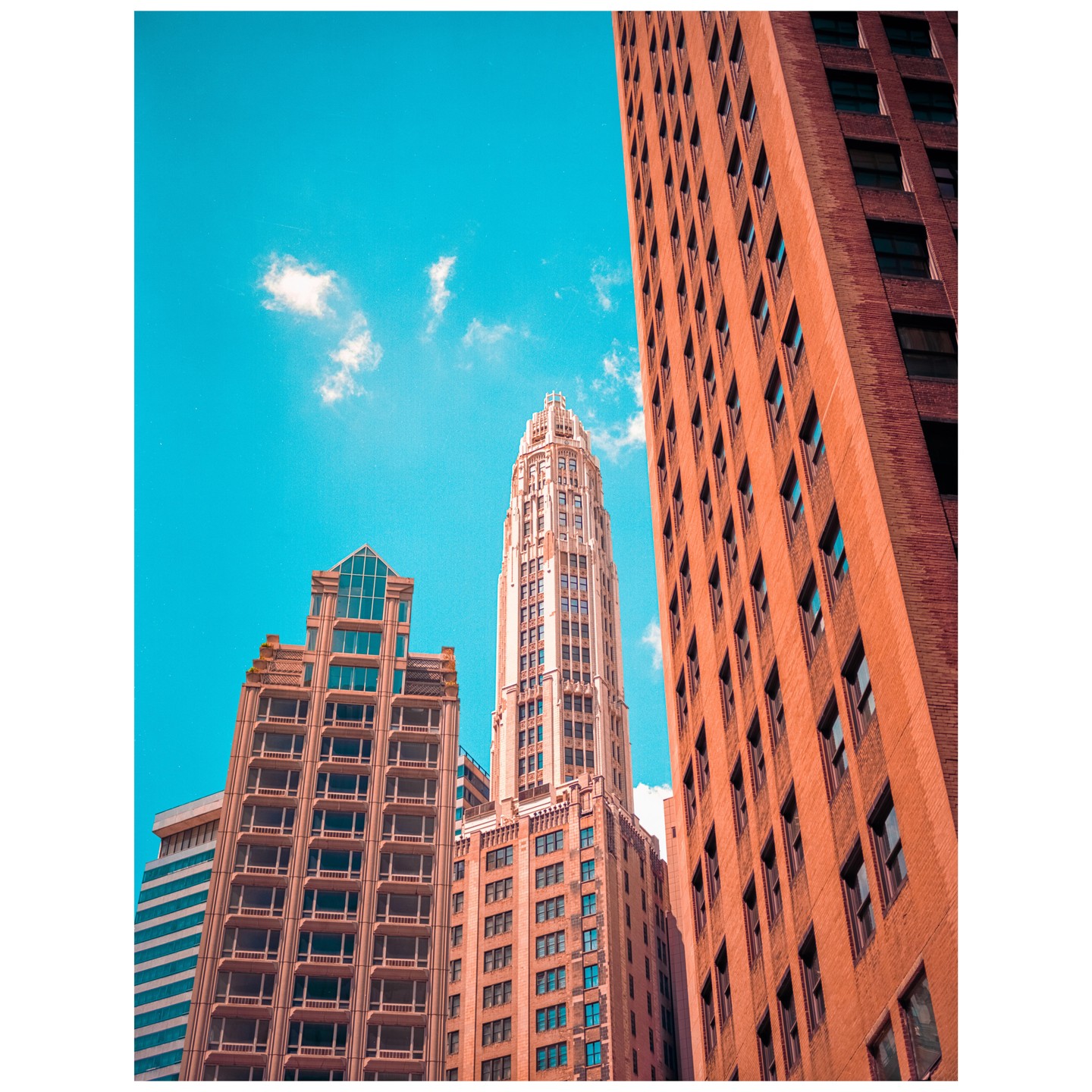 A low-angle view shows several tall buildings against a bright blue sky with a few clouds.