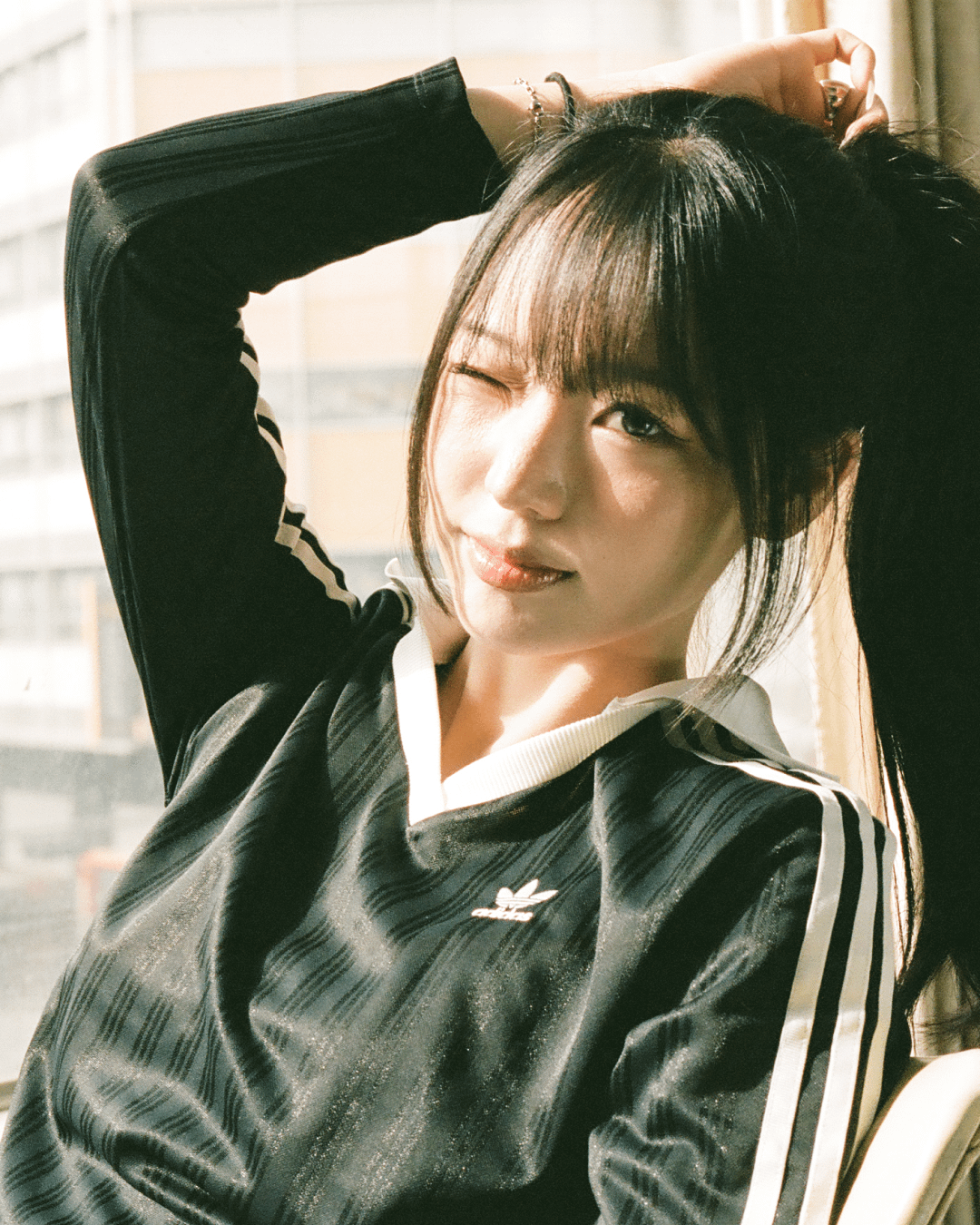 A woman winks at the camera while holding her hair up with both hands.