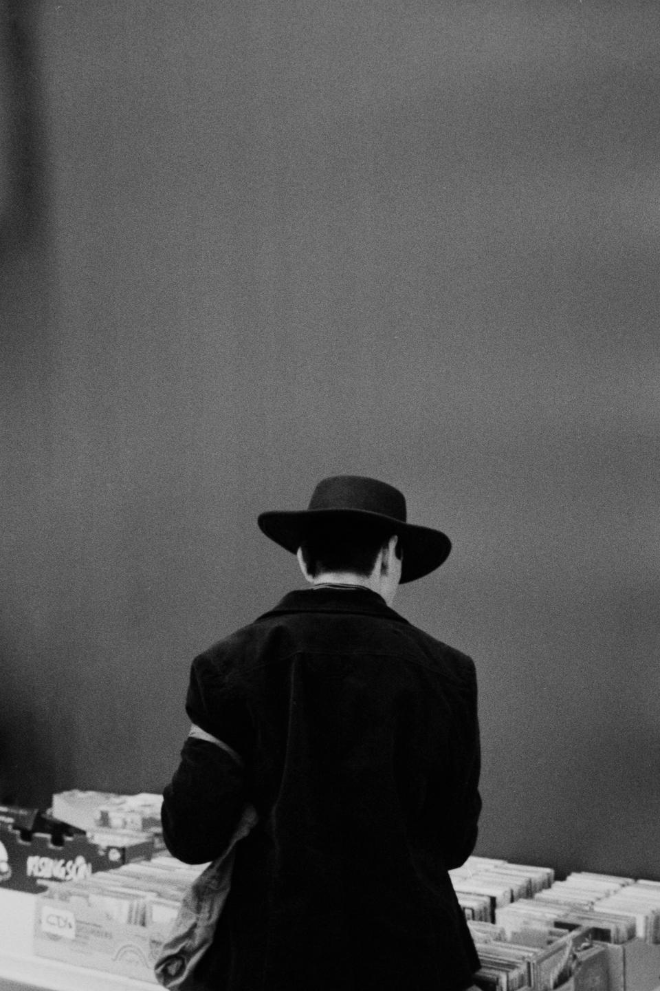 A man in a hat stands with his back to the viewer, looking at records.