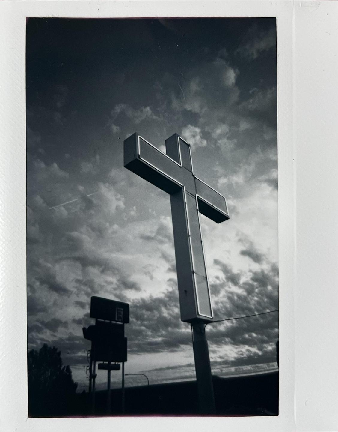 A large cross sign stands against a cloudy sky.