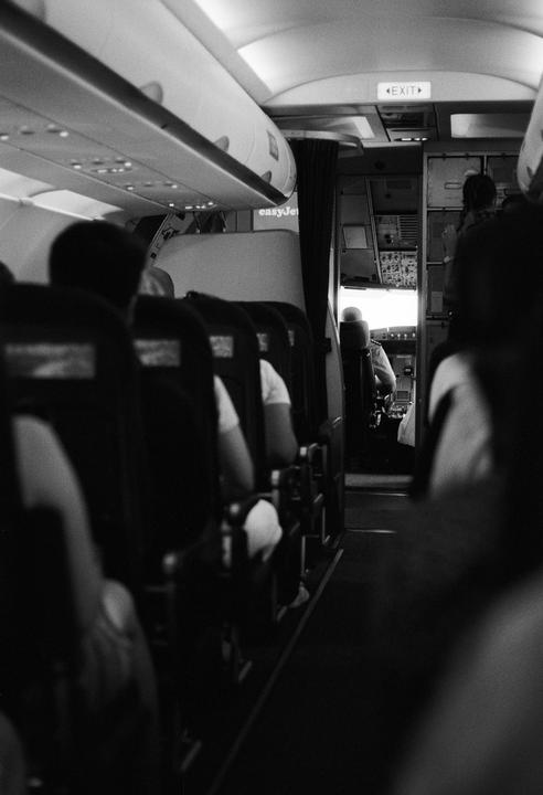 The interior of an airplane shows passengers seated and the cockpit visible at the front.
