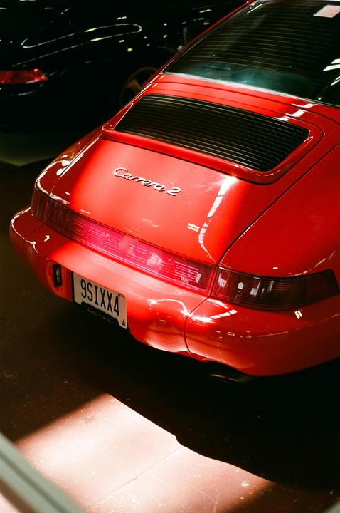 The rear of a red sports car with a license plate is illuminated by a bright light.
