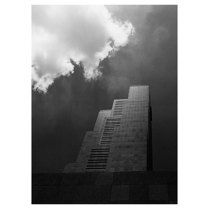 A tall, stepped building with a dark facade stands against a cloudy sky.