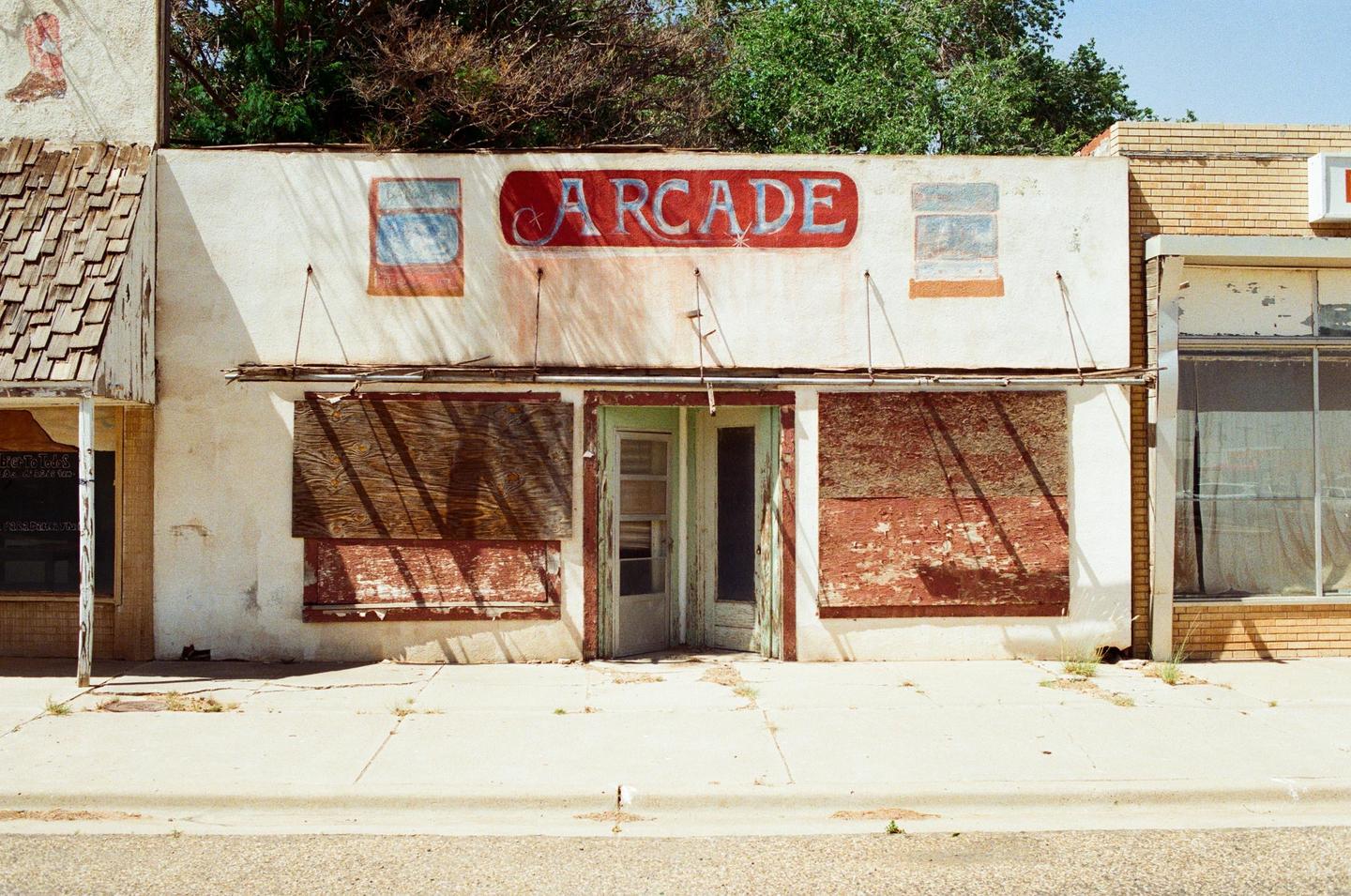 An abandoned arcade building with boarded-up windows and a faded "ARCADE" sign is visible from the street.