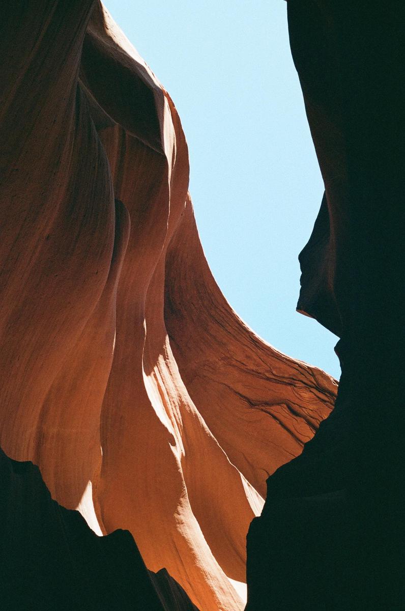 Light illuminates the wavy, orange rock formations of a slot canyon against a bright blue sky.