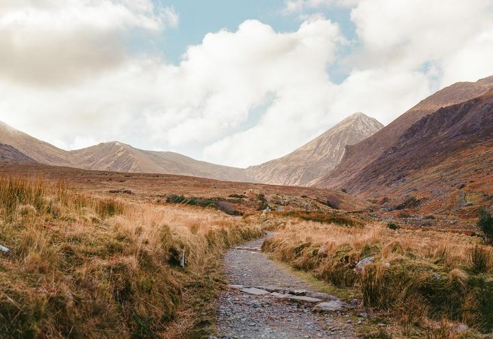 A rocky path leads through a valley with mountains on either side under a cloudy sky.