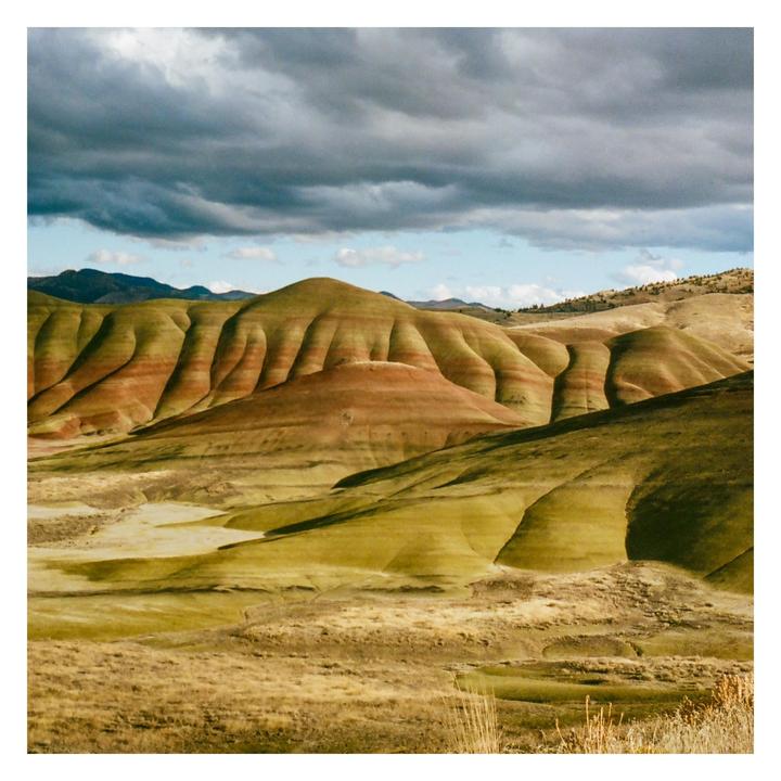 Rolling hills with colorful stripes are visible under a cloudy sky.