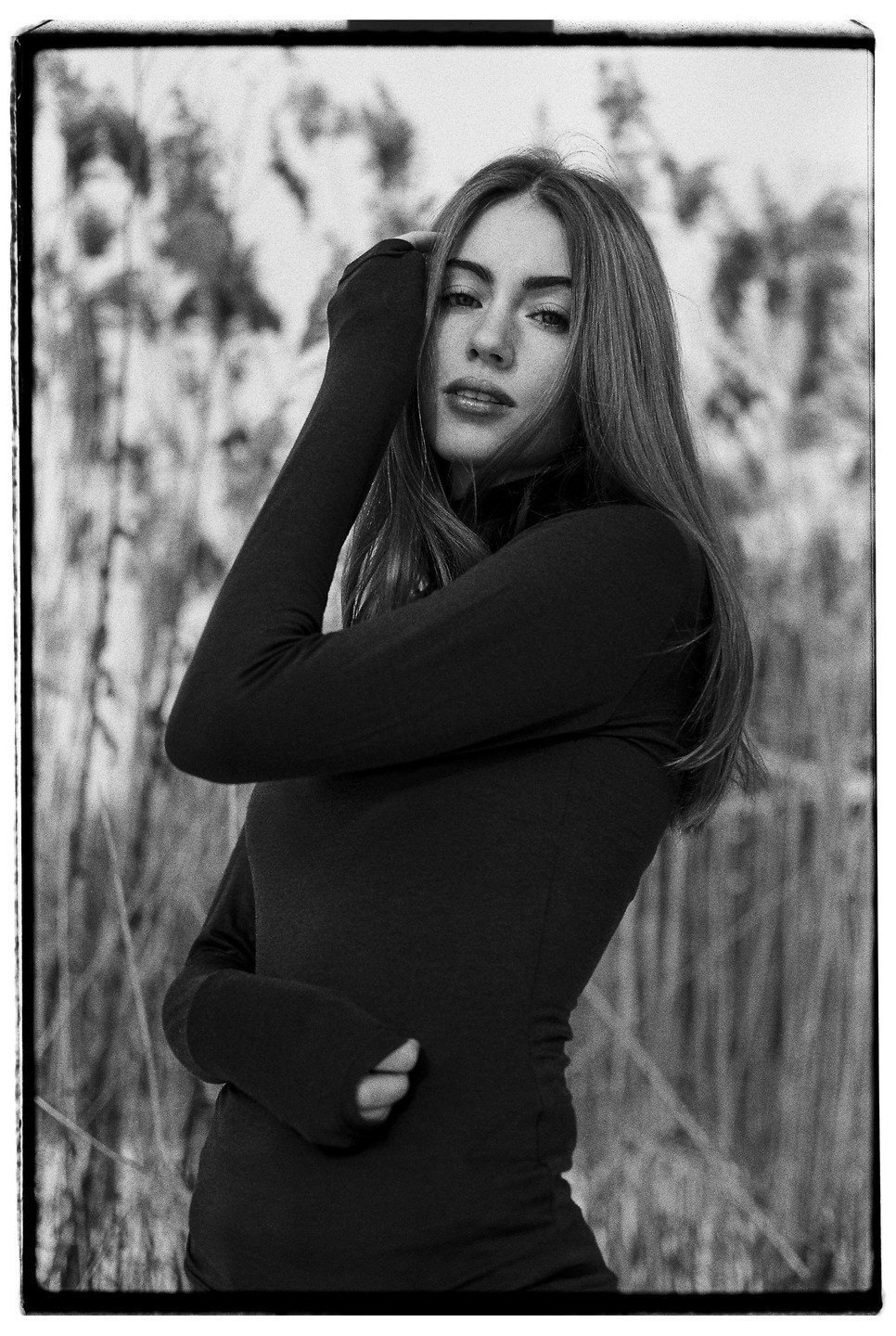 A woman with long hair poses in a field of tall grass.