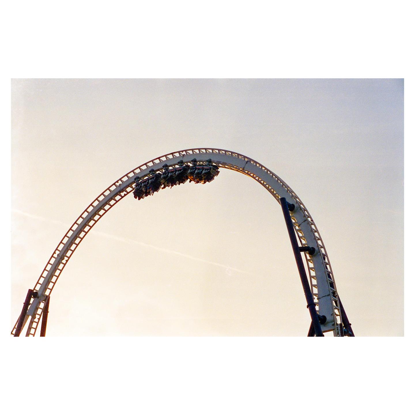 A rollercoaster car with people is upside down on a loop against a light sky.