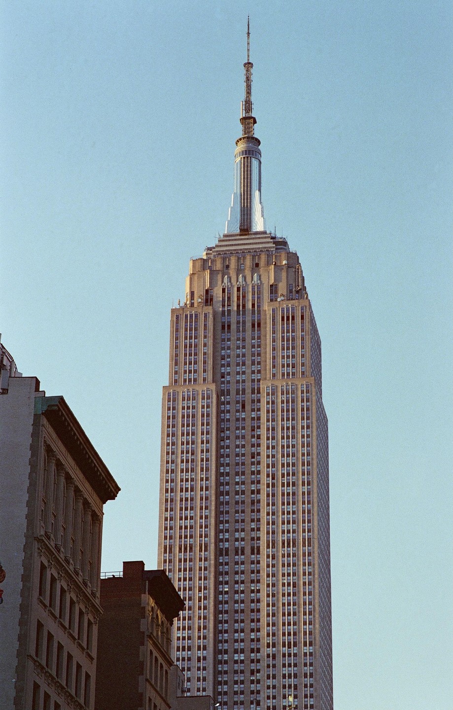 The Empire State Building stands tall against a clear sky, with other buildings visible in the foreground.