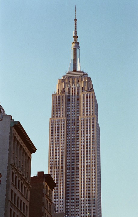 The Empire State Building stands tall against a clear sky, with other buildings visible in the foreground.