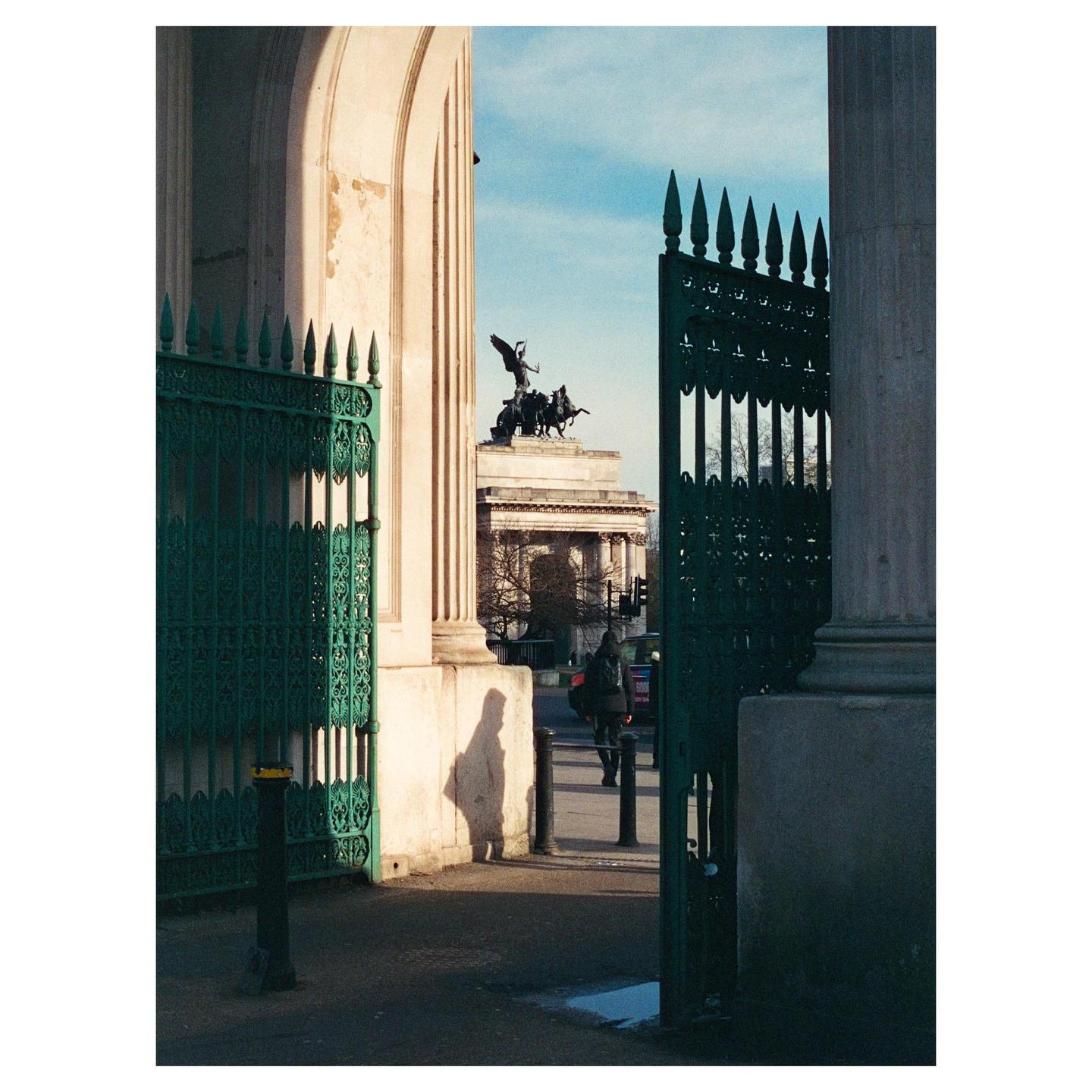 A person walks past a large green gate with a monument in the background.
