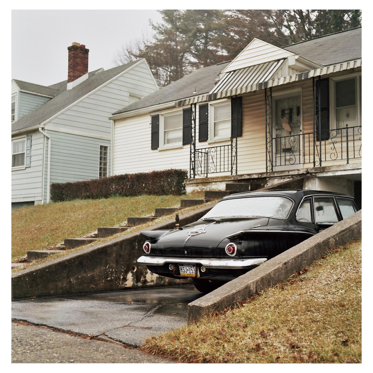 A black car is parked in a driveway in front of a house with a porch.