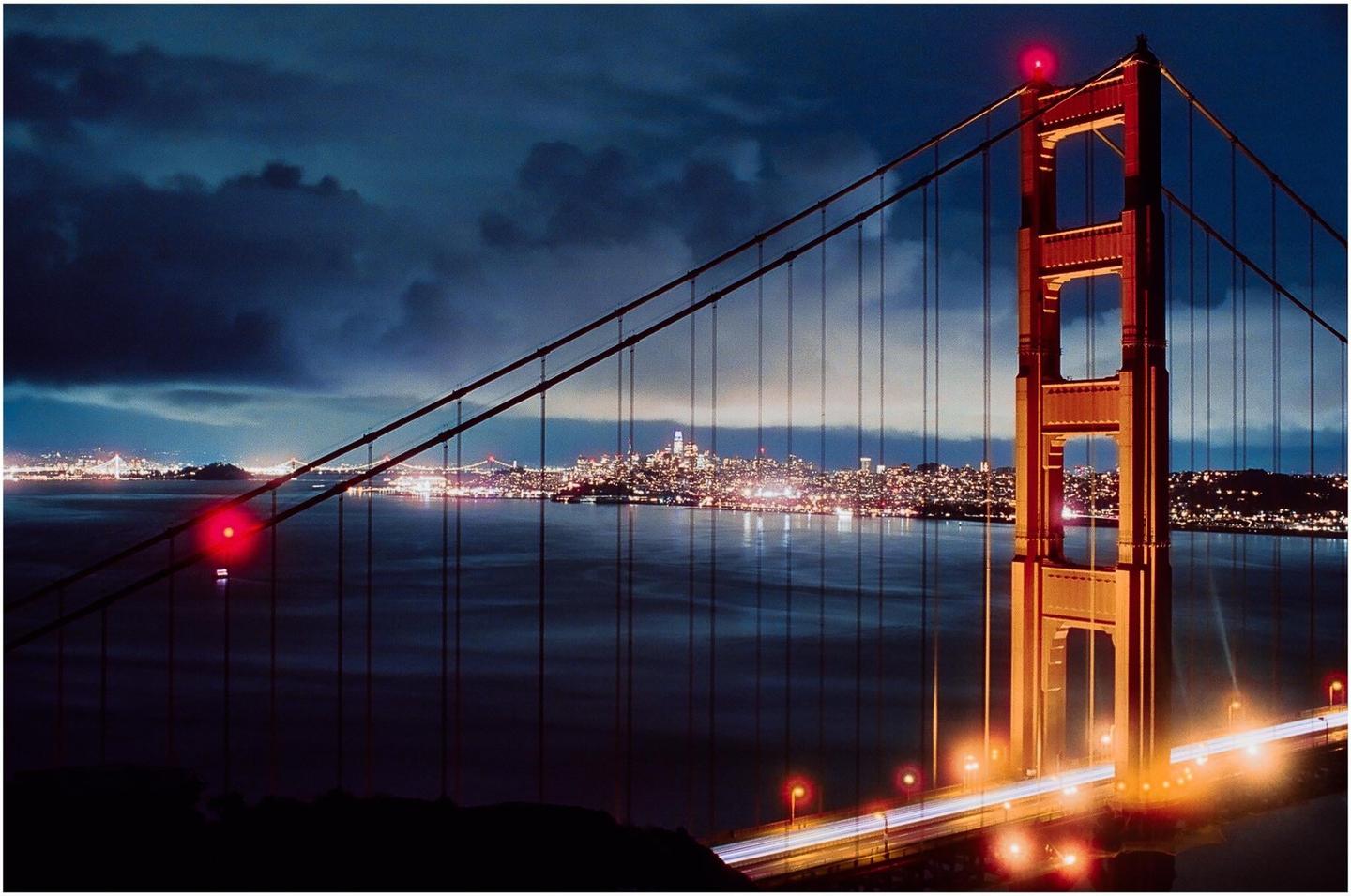 The Golden Gate Bridge is illuminated at night with the San Francisco skyline visible across the water.