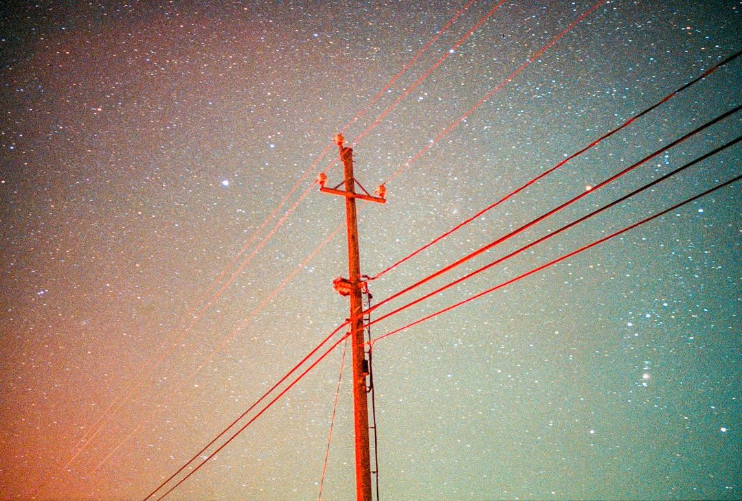 A utility pole with red wires stands against a starry night sky.