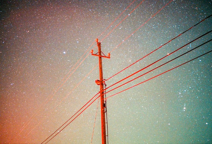 A utility pole with red wires stands against a starry night sky.