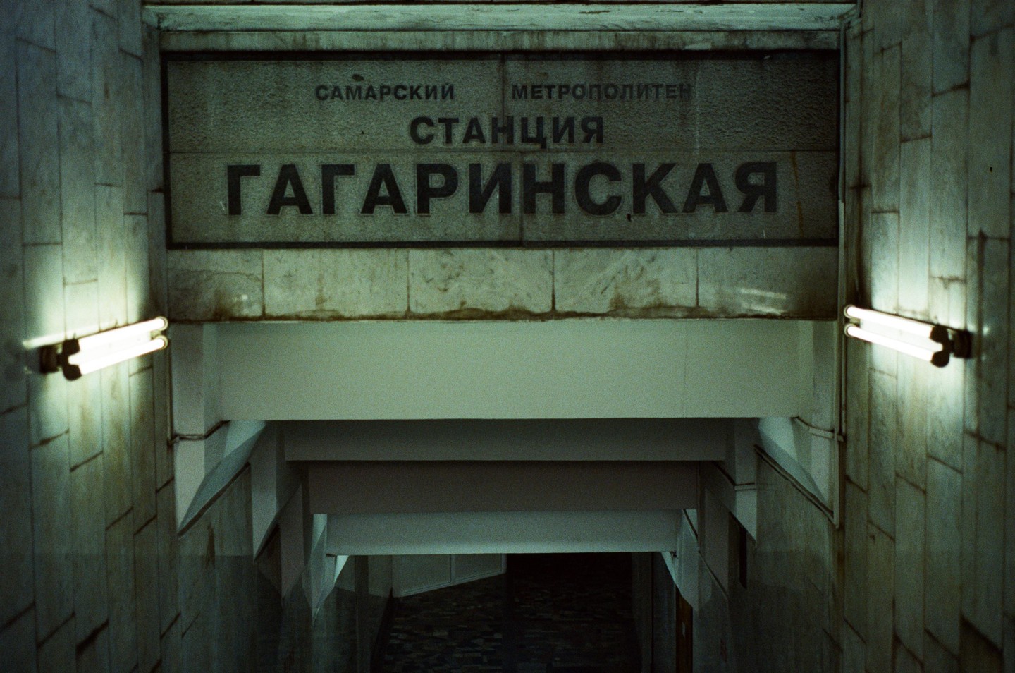 A sign for the Gagarinskaya metro station is mounted above a dark stairwell with fluorescent lights on either side.