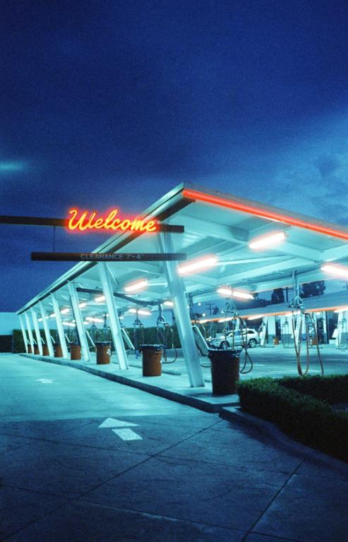 A neon "Welcome" sign illuminates a car wash at night.