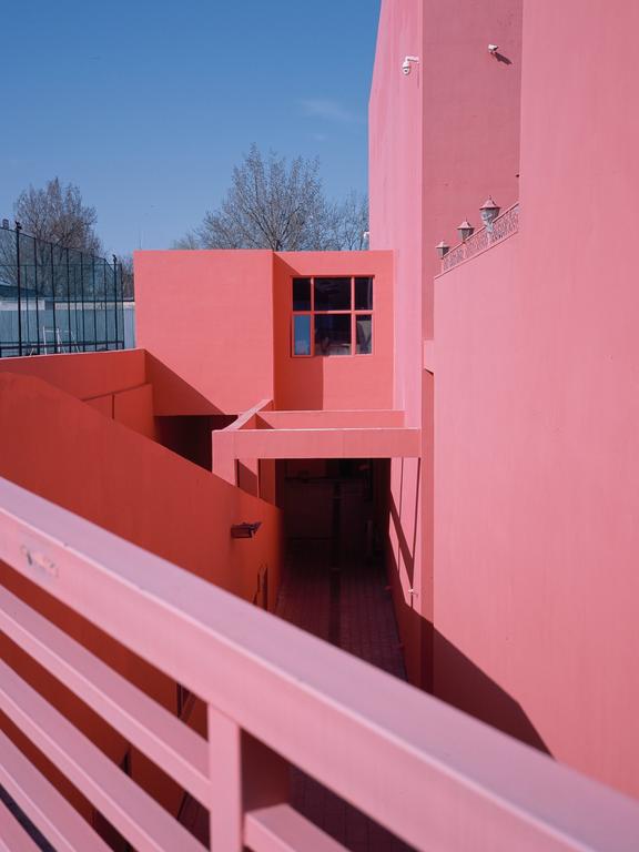 A pink building with a window and a railing is shown under a clear blue sky.