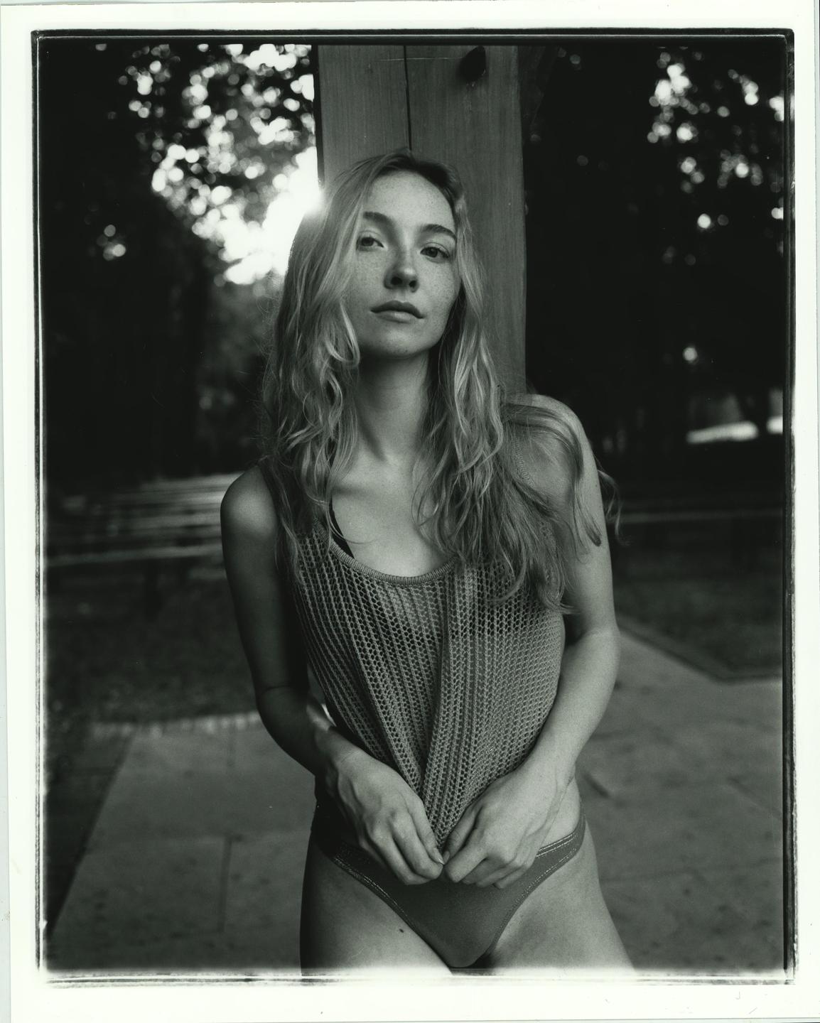 A woman with long hair and freckles stands outdoors, backlit by the sun.