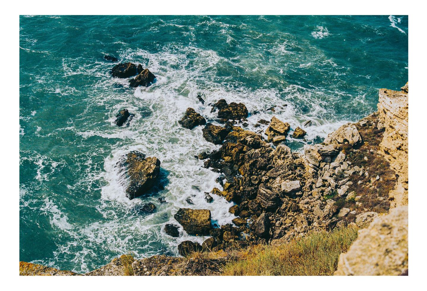Waves crash against rocks at the base of a cliff.