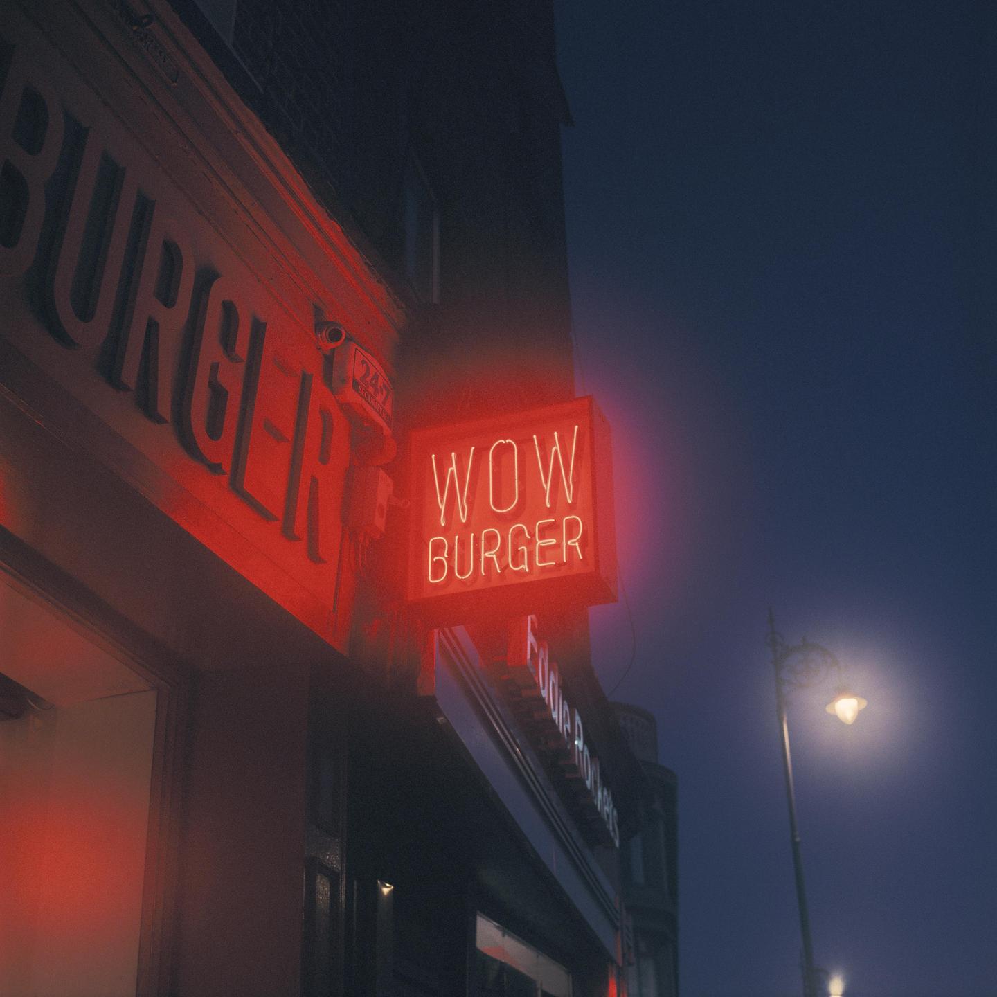 A red neon sign for "Wow Burger" is illuminated on a building at night.