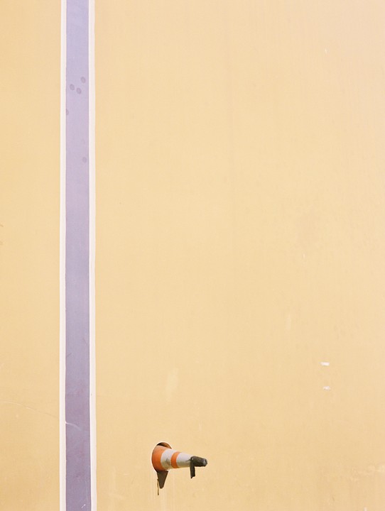 A yellow wall with a purple stripe and a small orange and white cone protruding from a hole.