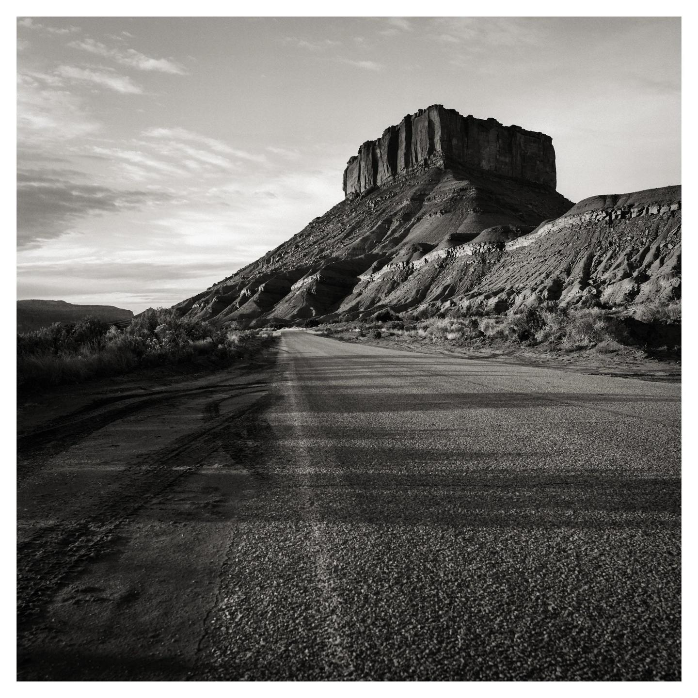 A road leads towards a large mesa under a cloudy sky.