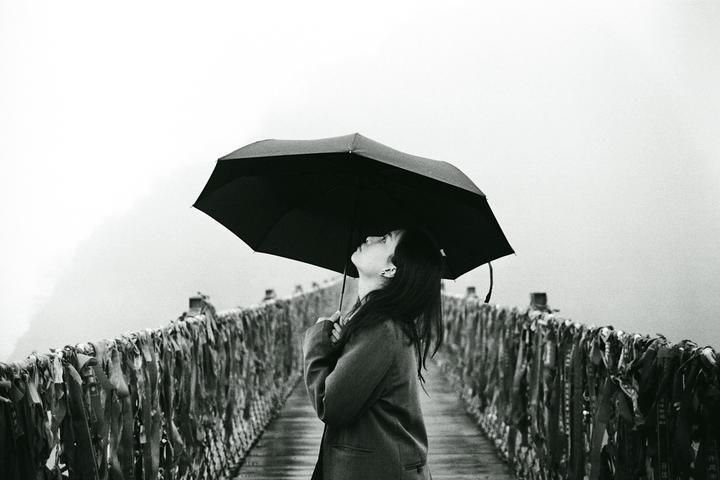 A woman holding an umbrella looks up while standing on a bridge adorned with ribbons.