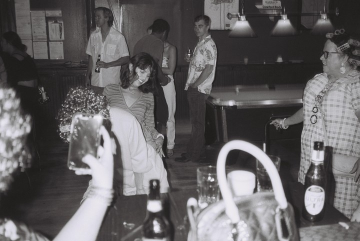 A group of people are gathered in a dimly lit bar with a pool table in the background.