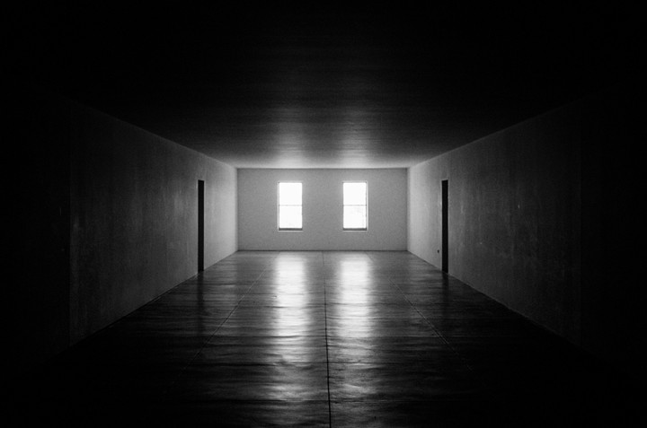 A long, empty, dark hallway leads to two bright windows at the far end, with light reflecting on the floor.